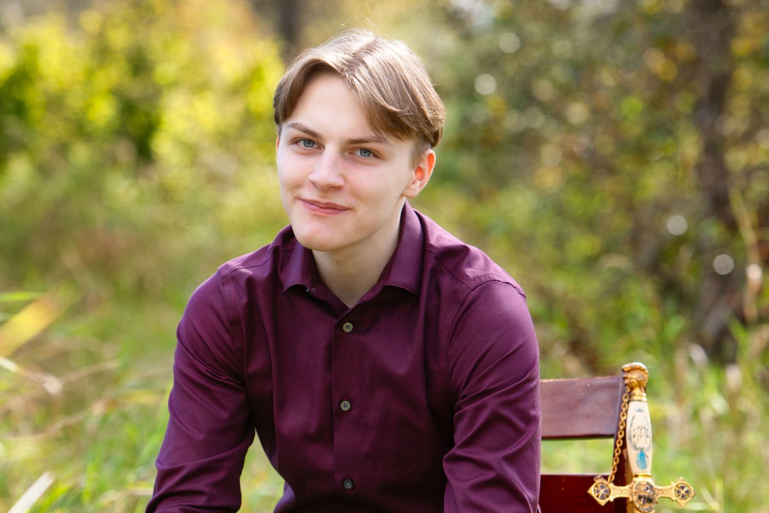 Portrait of person in burgundy shirt seated outdoors with natural background.