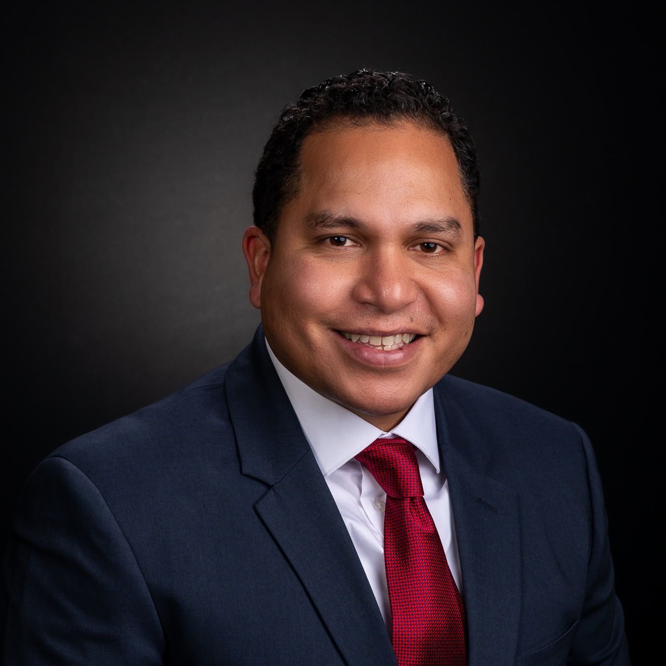 Retiring service member studio portrait blue suit, red tie, vignetted black background