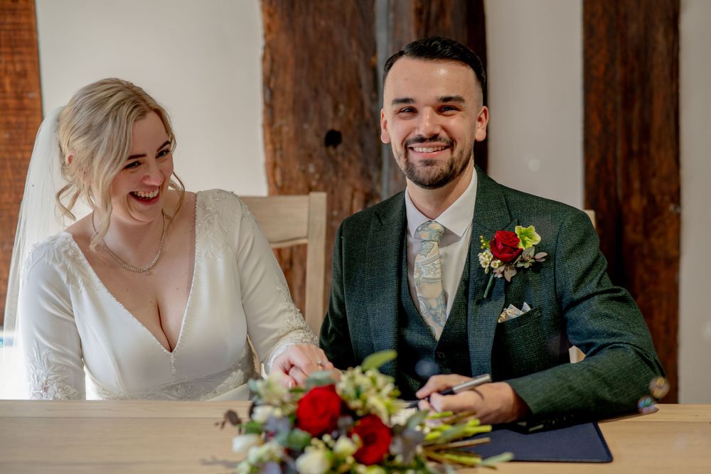 A couple sits at a decorated ceremony table with red floral arrangements.