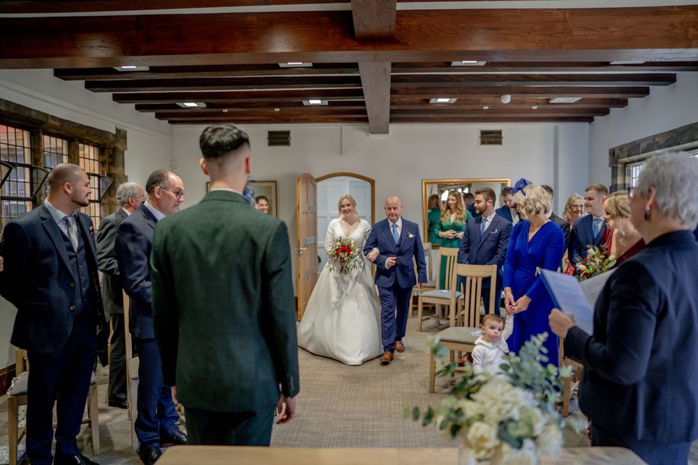 An intimate wedding ceremony takes place in a rustic room with wooden beams and guest seating.