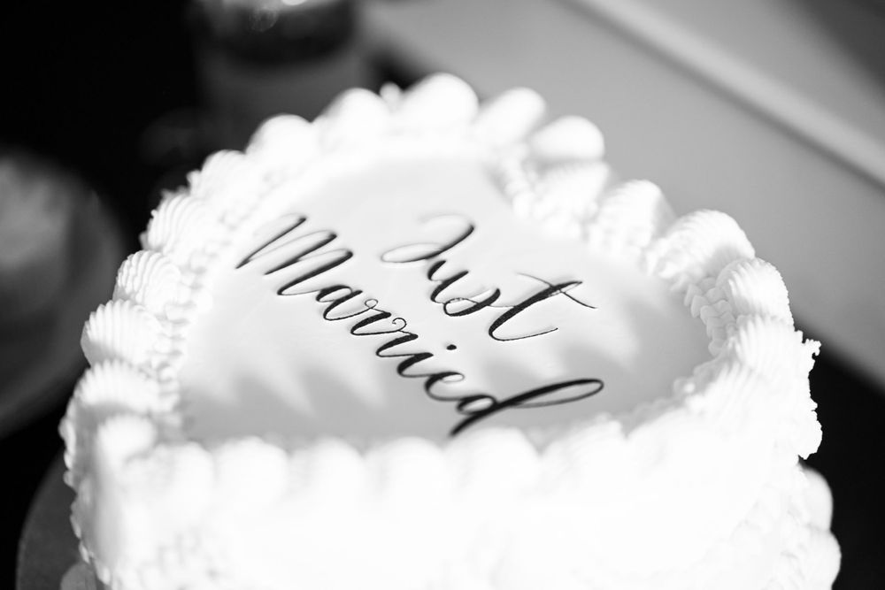 Black and white close-up of a wedding cake with 'Just Married' text written in cursive script and decorative piping.