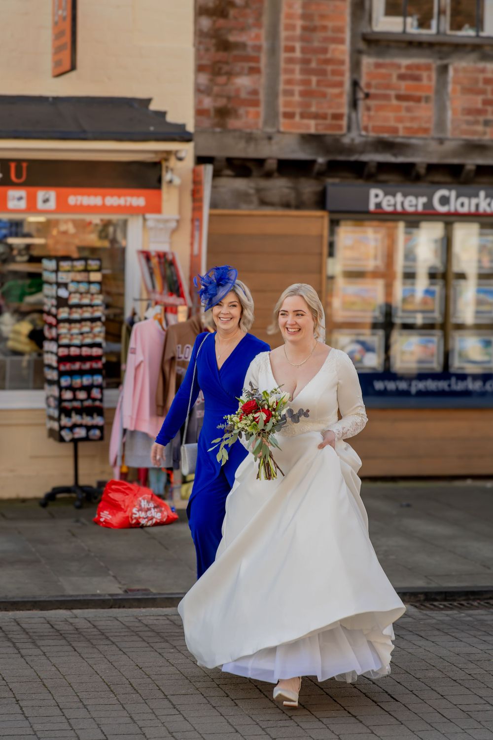 A wedding scene outside shops with someone in a flowing white bridal gown and another in a vibrant blue dress walking.