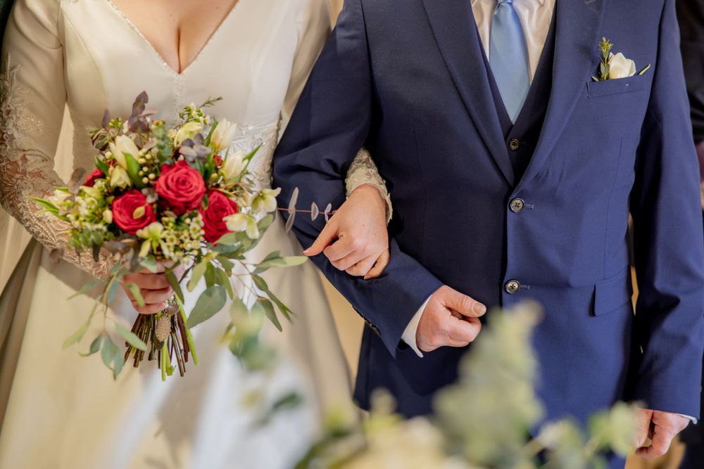 Close-up of bride in white dress holding colorful bouquet next to groom in navy suit with boutonniere.