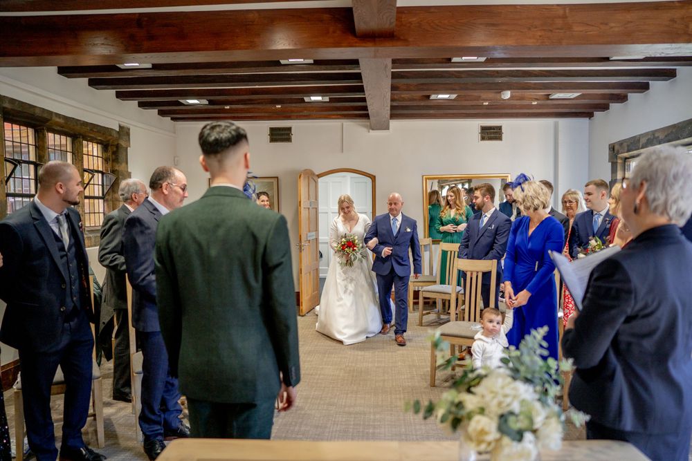 Indoor wedding ceremony at a rustic venue with exposed wooden beams and guests gathered in formal attire.
