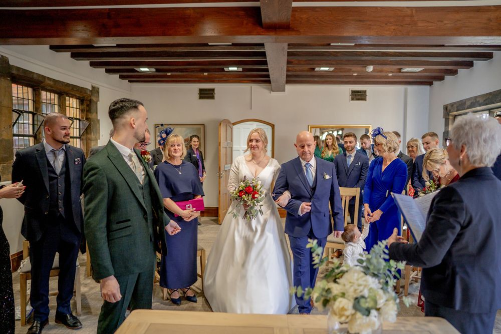 Wedding ceremony taking place in a rustic room with exposed wooden beams and natural light.