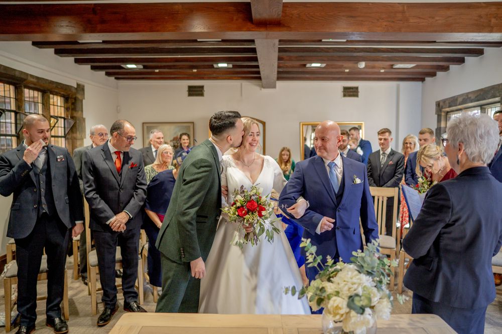 Wedding ceremony taking place in a rustic venue with exposed wooden beams and guests gathered around the couple.