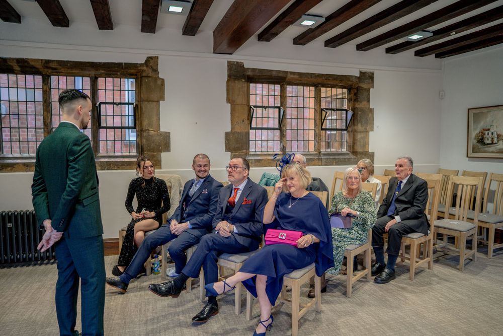 A group of guests seated on wooden chairs at a rustic indoor venue with exposed wooden beams.