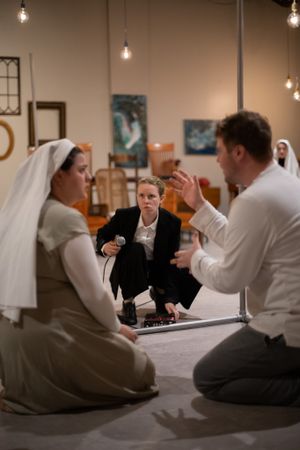 Theatrical performance taking place on floor with hanging lights and religious imagery in background.