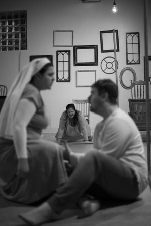 Black and white shot showing people having conversation in room with vintage frames on wall.