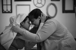 Black and white intimate theatrical scene showing two performers in close embrace.