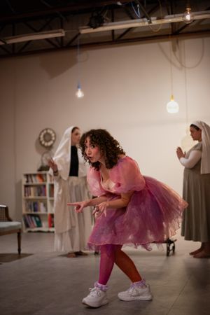 A dancer in a pink tutu dress performs energetically while others observe in the background.