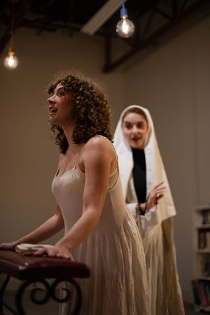 Dramatic theatrical scene with performers in period costume under moody hanging lights.