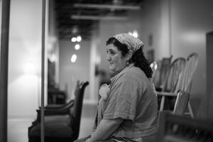 Black and white portrait of someone sitting in an empty church auditorium.