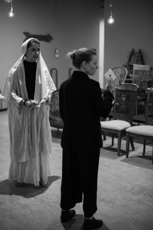 Monochrome image of two performers in costume during theatrical scene with dramatic lighting.