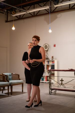Two performers in black attire standing in industrial-style performance space with hanging lights.