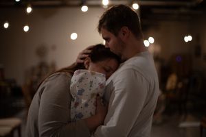 Two people share an intimate embrace under soft decorative lighting in an indoor venue.