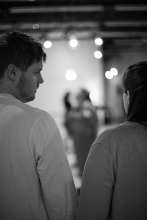 Two figures stand in silhouette against a blurred background with bokeh lights.
