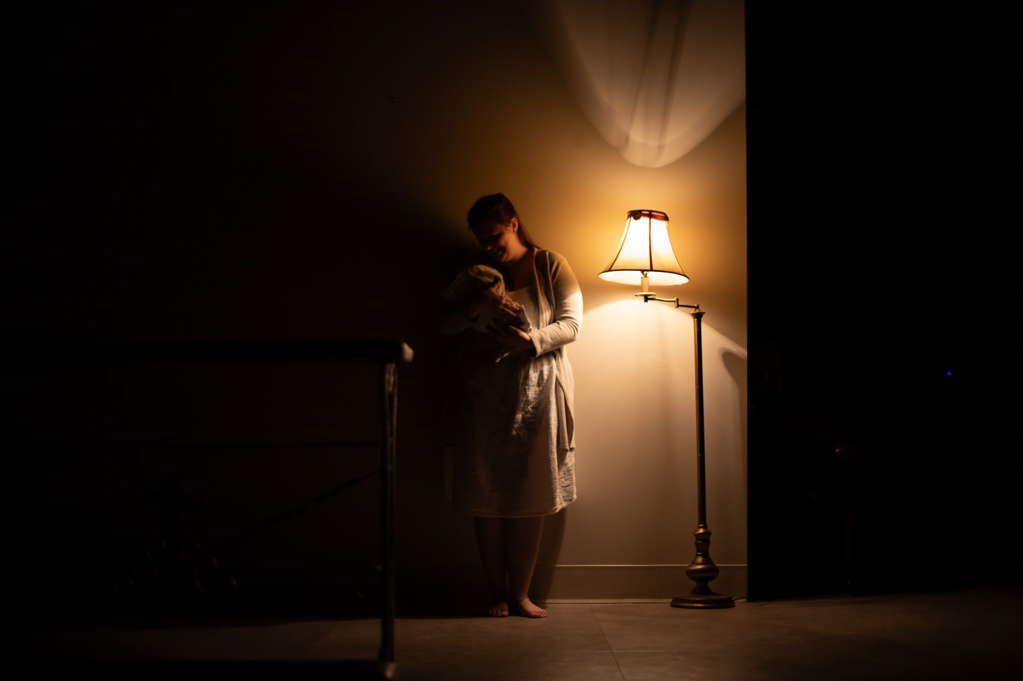 A silhouetted figure stands beside a glowing floor lamp in a darkened room.
