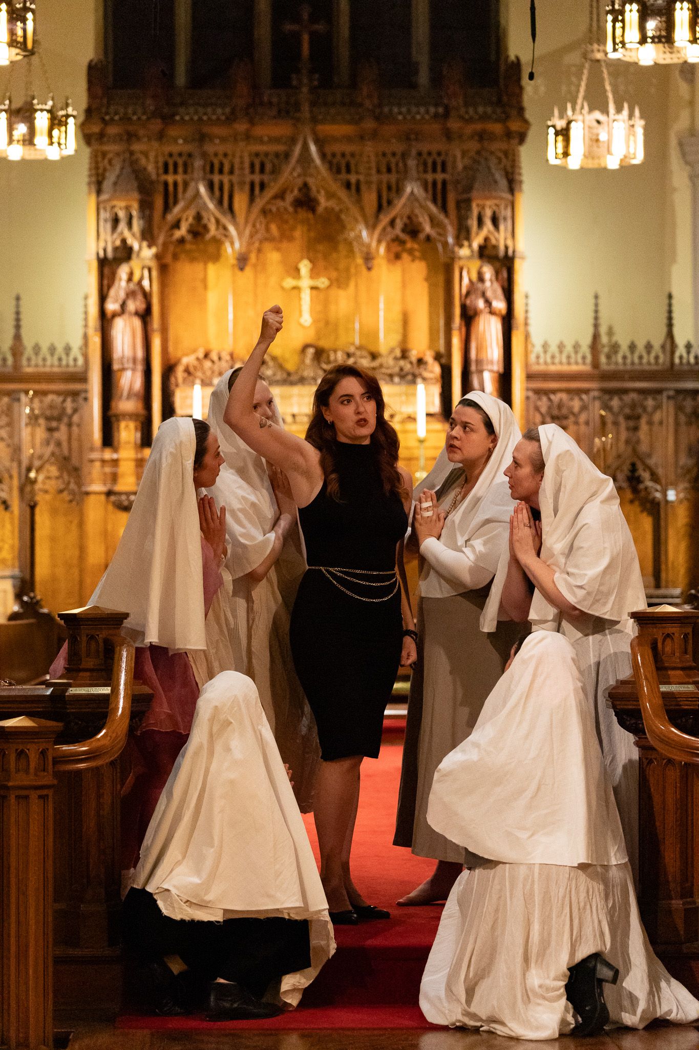 People in religious attire gather inside an ornate church with gothic architecture and warm lighting.
