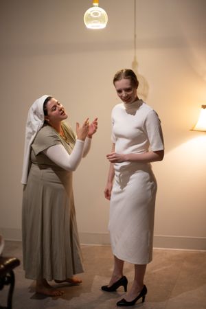 Two performers in white and beige outfits engage in an expressive theatrical scene under warm lighting.