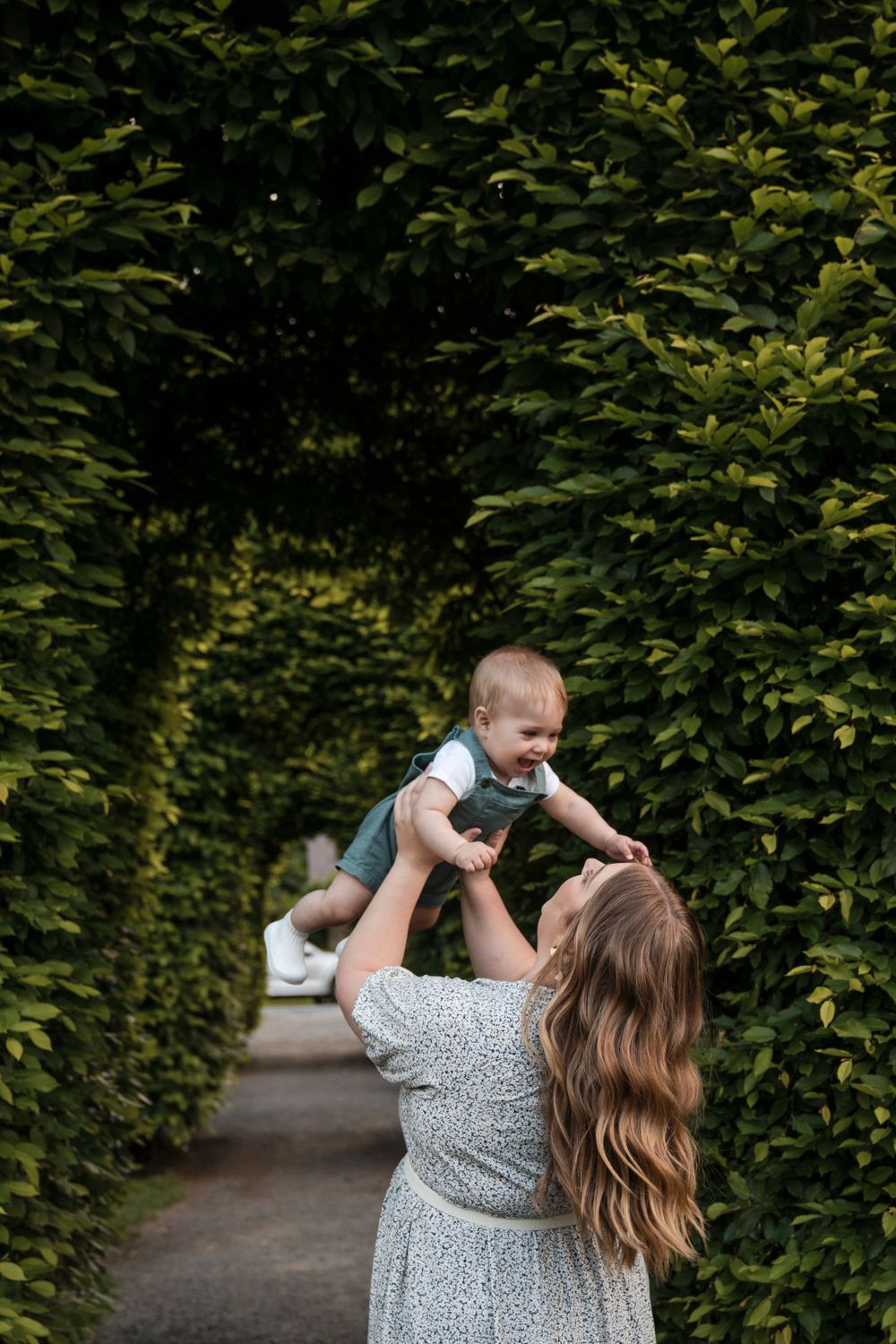 A joyful moment captured in a garden pathway lined with green hedges, showing playful interaction and lifted spirits.