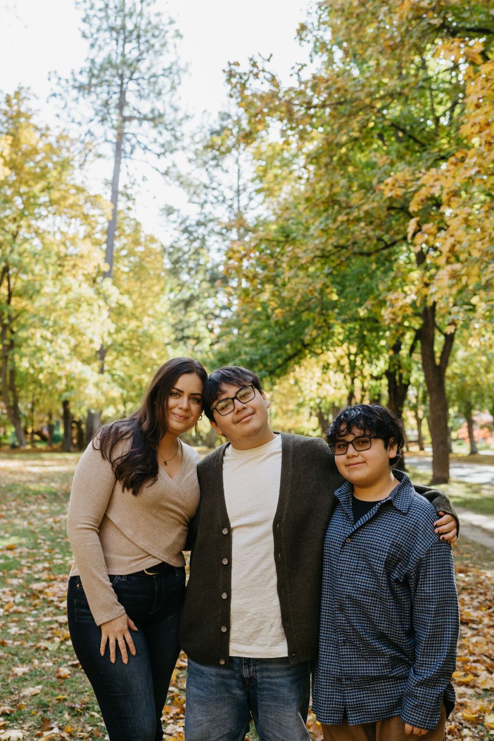A group stands together outdoors in a park during autumn with yellow and green trees in the background.