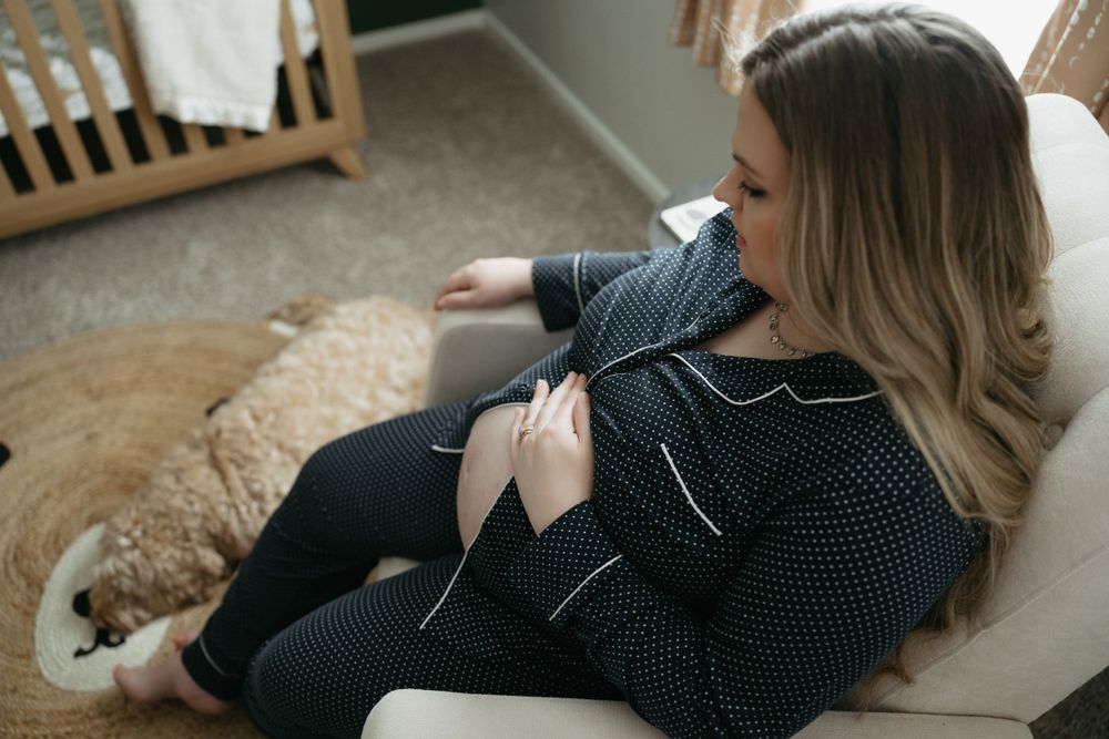 Person relaxes in chair wearing polka dot shirt while knitting with yarn and needles.