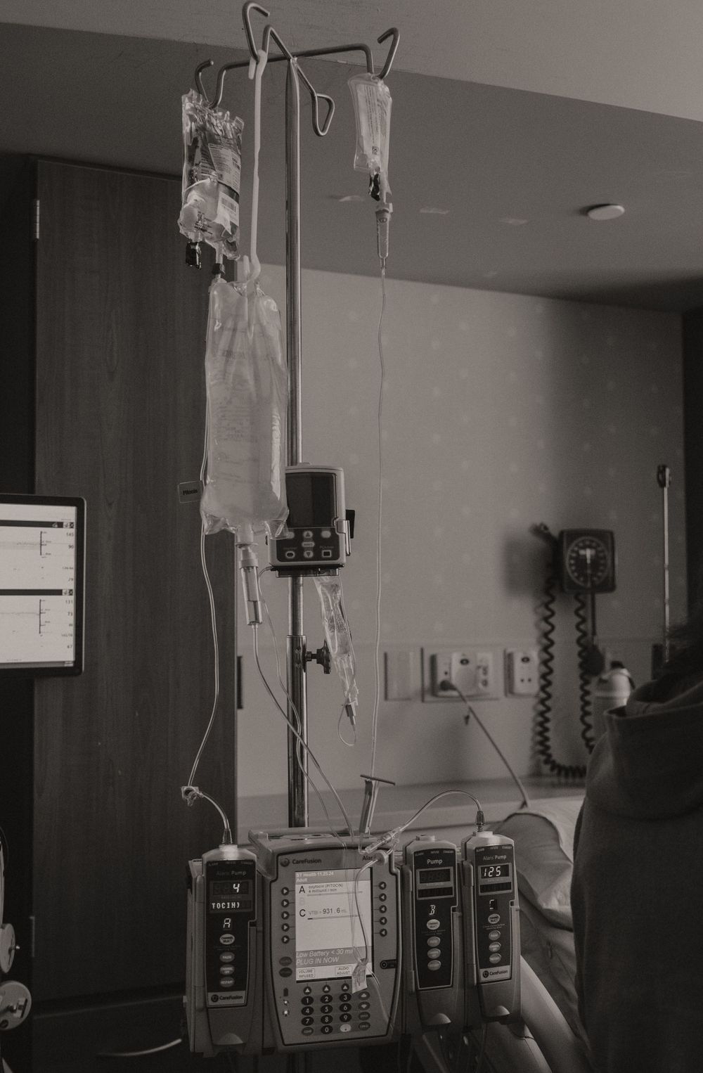 Hospital room interior with IV poles and medical equipment against a grey wall.