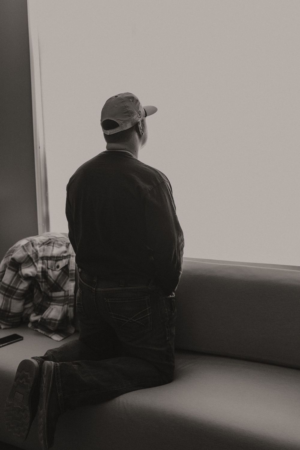 Person sitting on hospital bed viewed from behind in monochrome.