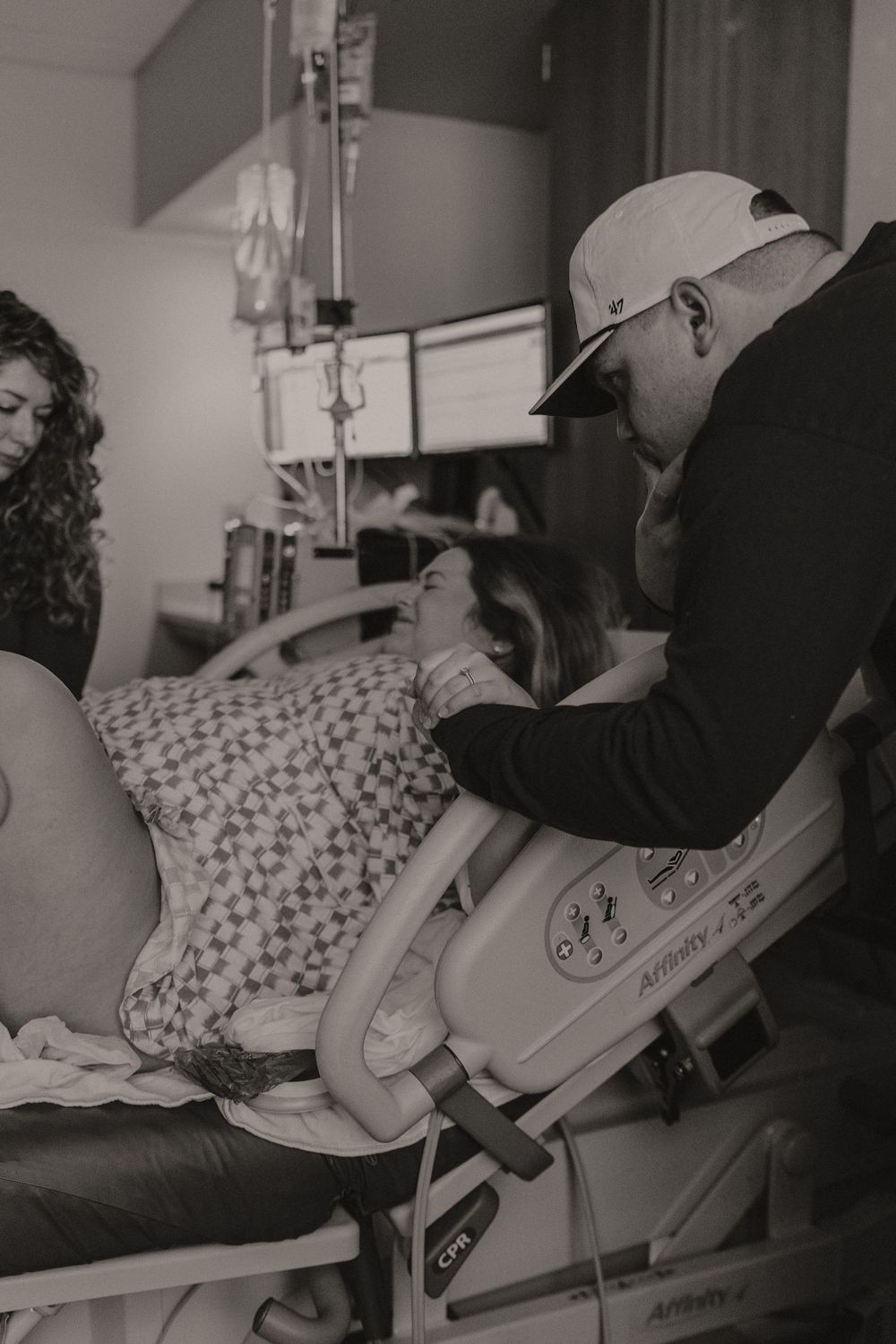 Black and white photo showing patient in hospital bed with medical equipment and IV drip.