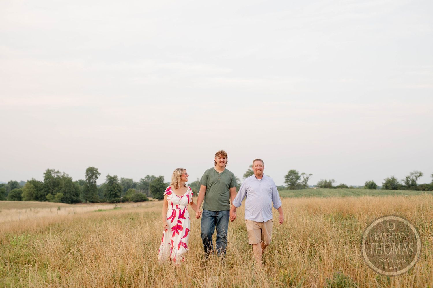 Family portrait of three people standing in a summer field during golden hour.