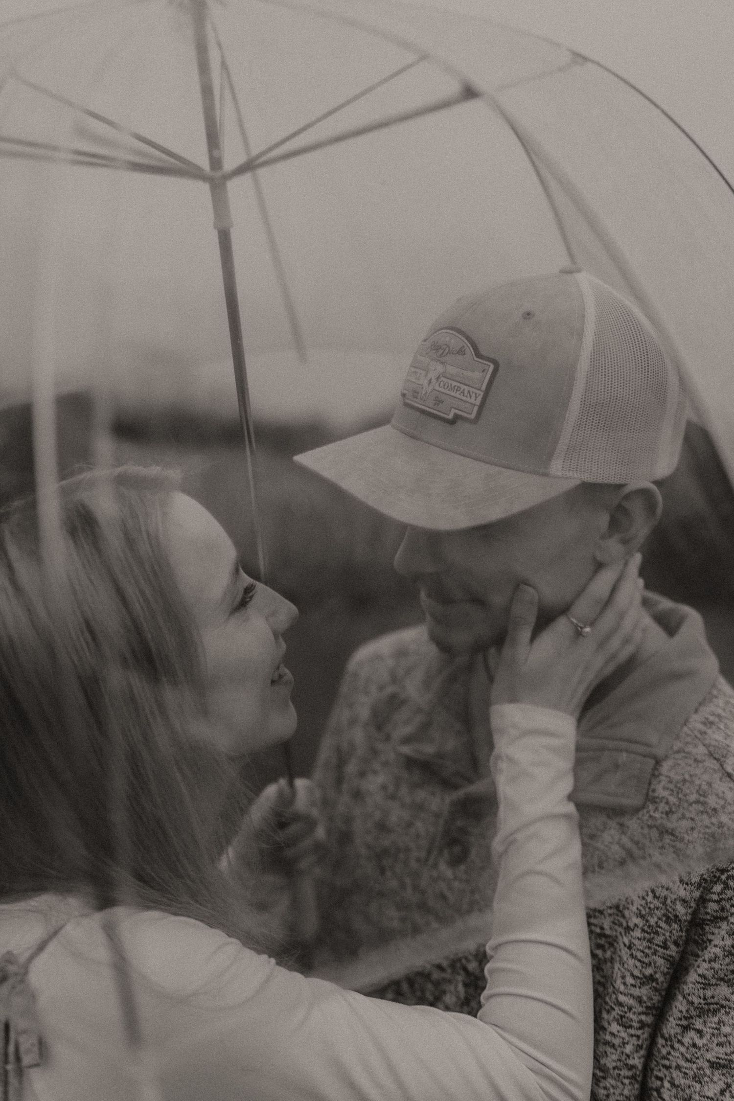 Black and white photo of couple sharing intimate moment under umbrella.