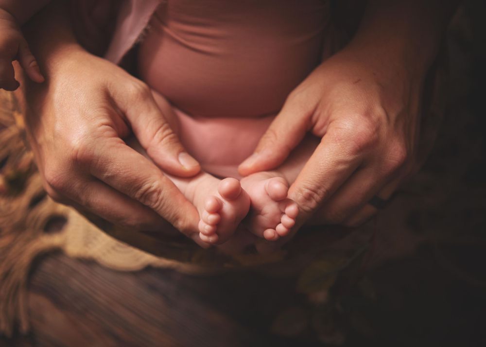 Adult hands gently holding tiny baby feet in a warm-toned intimate photograph.