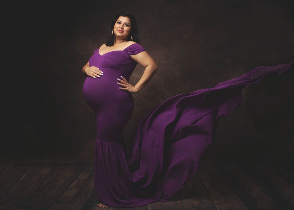 Dramatic maternity portrait in flowing purple gown against dark background.