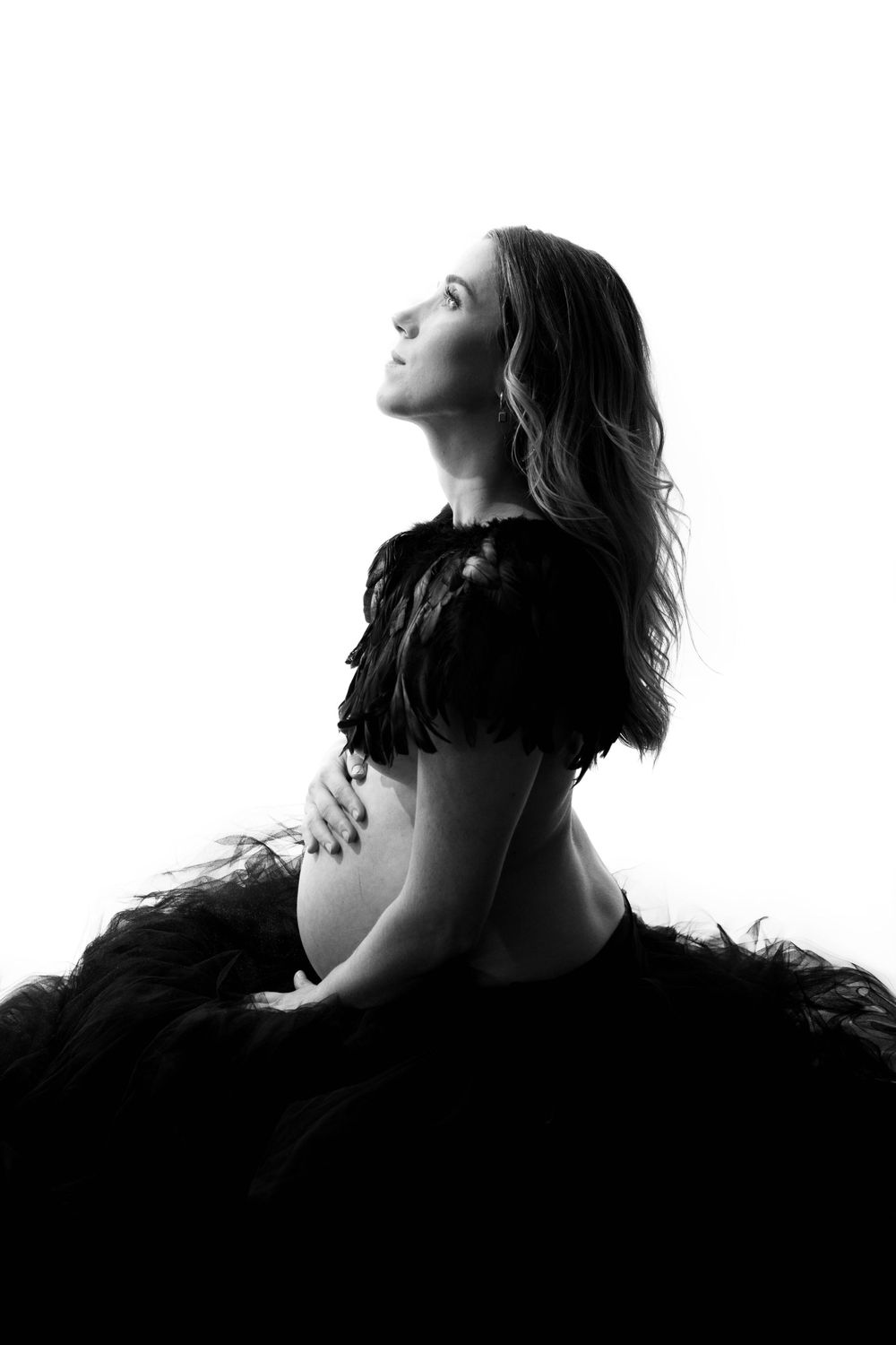 Silhouette maternity portrait in black featuring dramatic side profile pose.