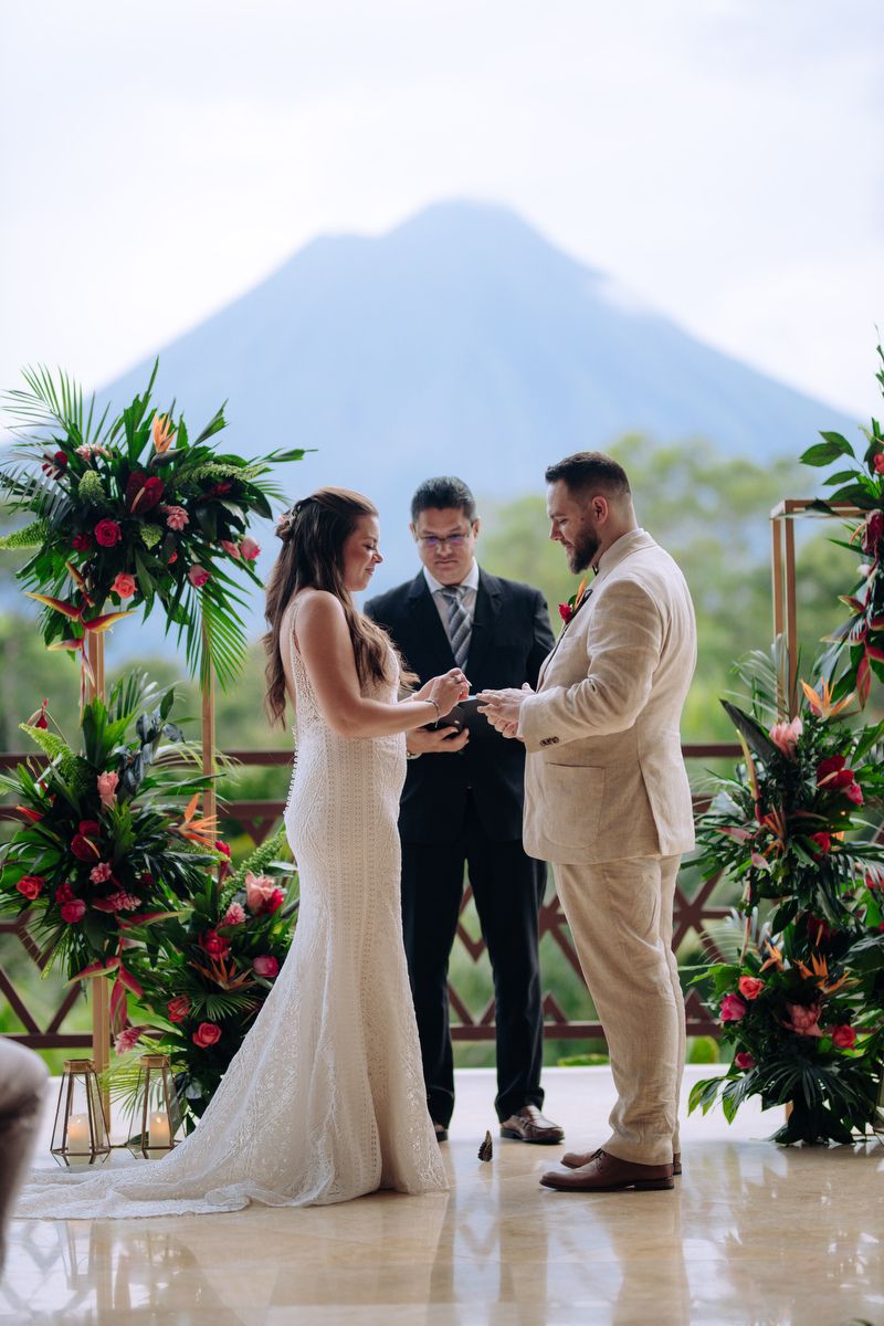 Wedding ceremony taking place with tropical floral arch and majestic volcano mountain vista in background.