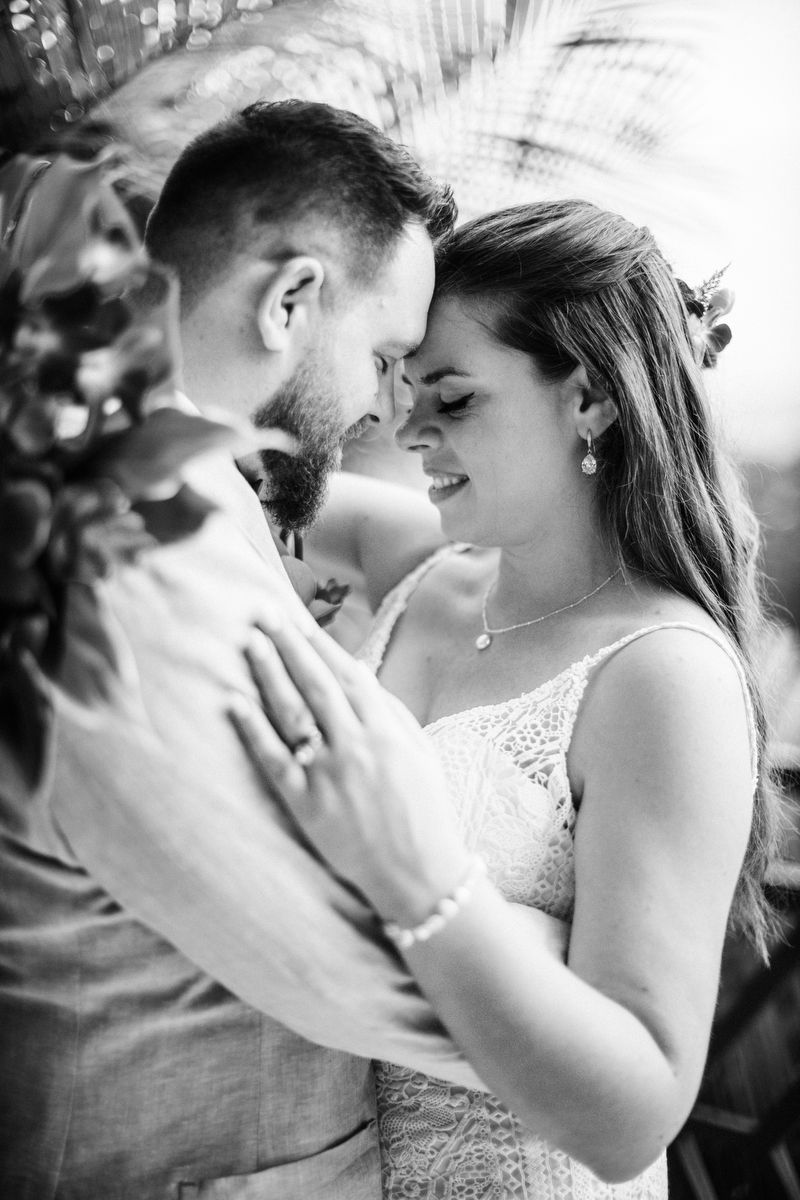 A tender black and white wedding portrait shows a couple sharing an intimate moment outdoors.