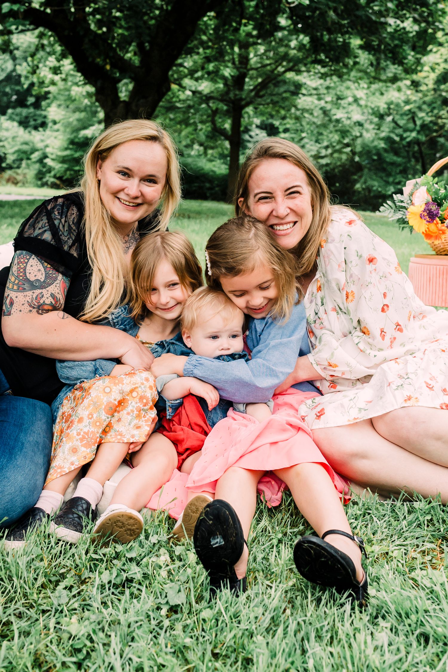 Group sitting together on green grass having fun during outdoor spring photoshoot with colorful dresses and flowers.