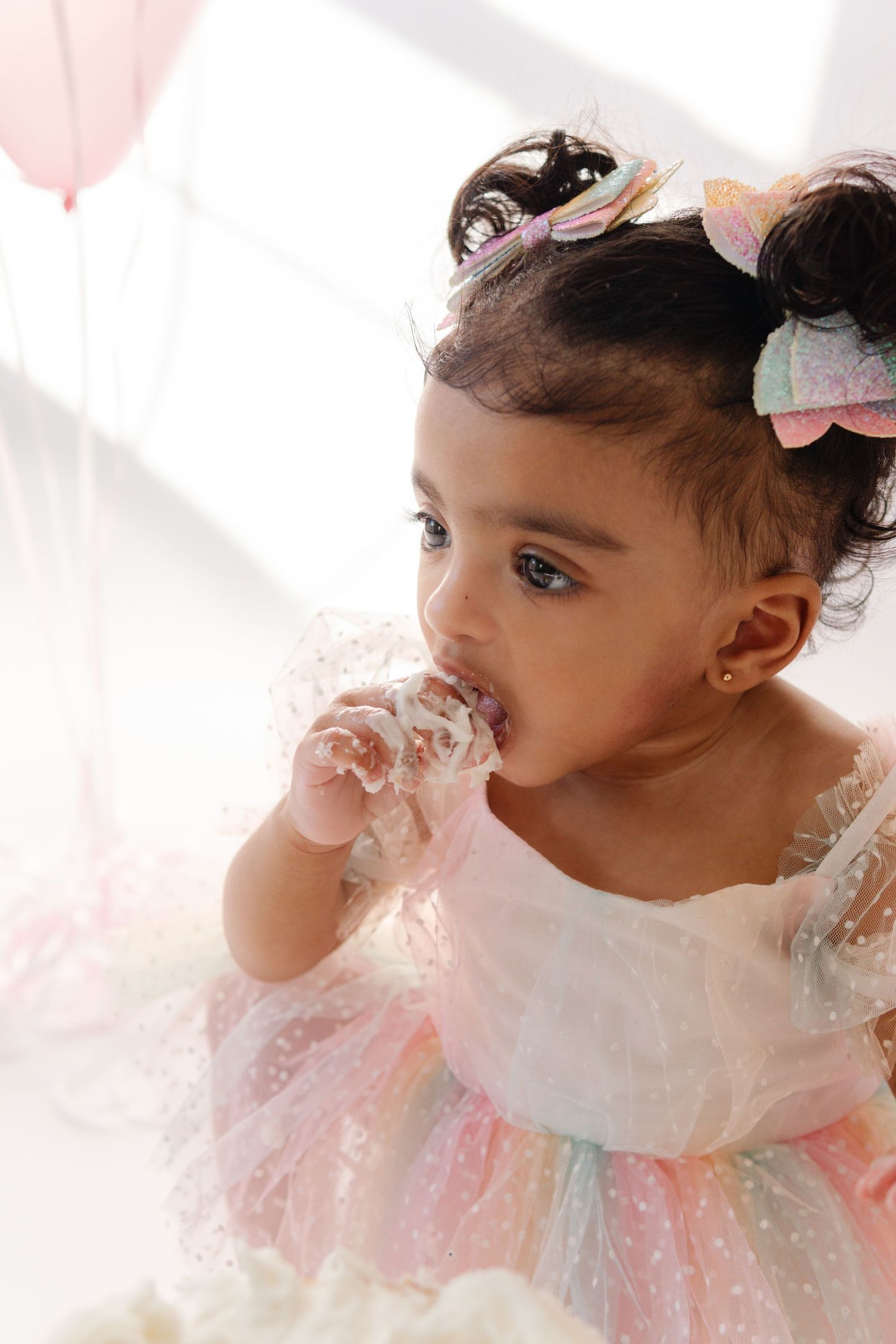A small toddler in a pastel tulle dress looks to the side while eating at a party setting.