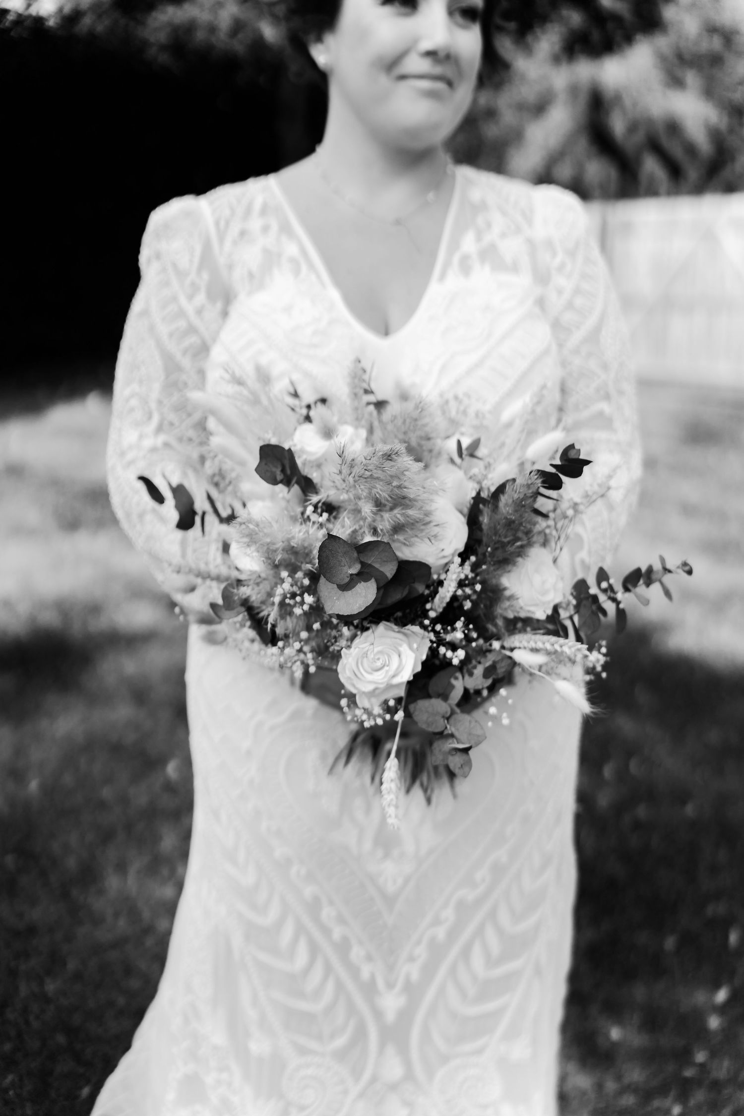 A bride in a white lace wedding gown holds a romantic bouquet of white and blush flowers in black and white photography.