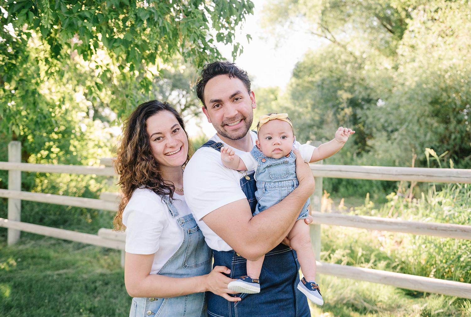 A family enjoys a sunny afternoon together outdoors near a wooden fence in a lush green setting.