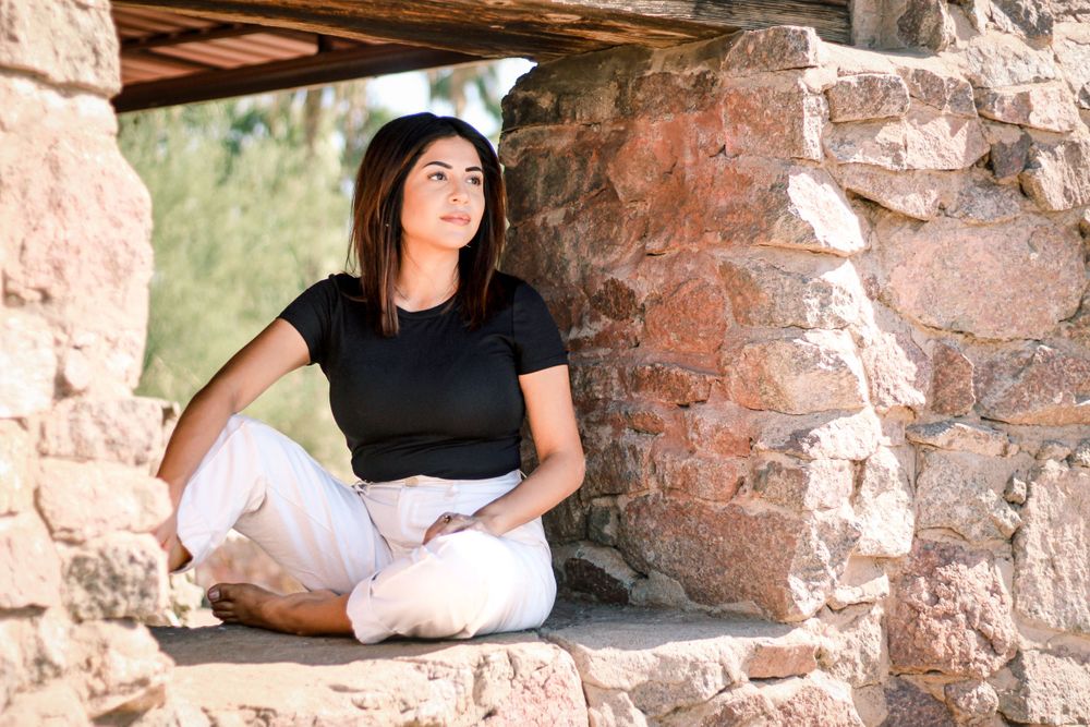 Portrait of person in black shirt and white pants sitting in rustic stone archway.