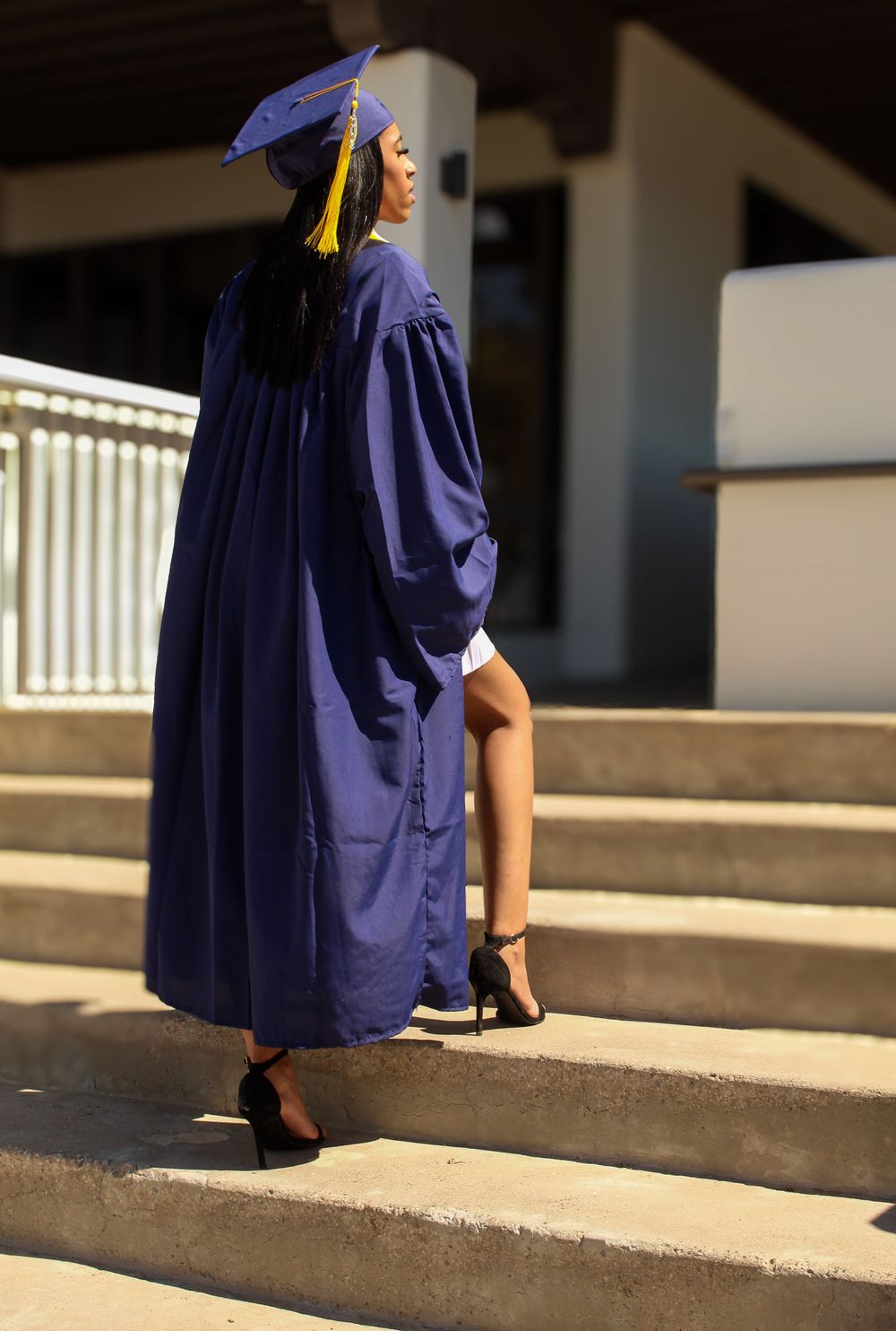 Side view of graduate in navy blue graduation gown ascending concrete steps.