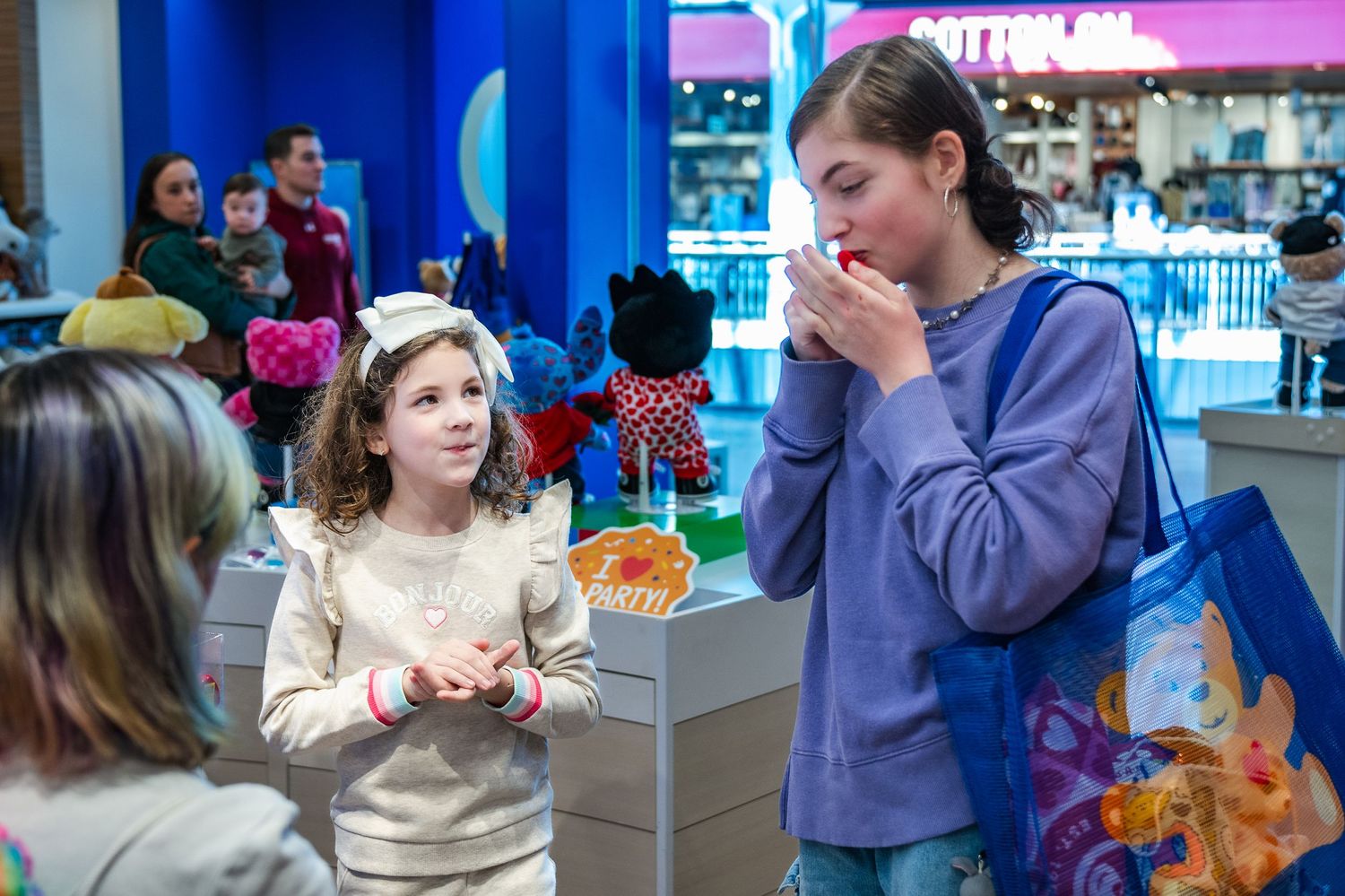 People talk while standing near a mall food court with bright purple lighting in the background.