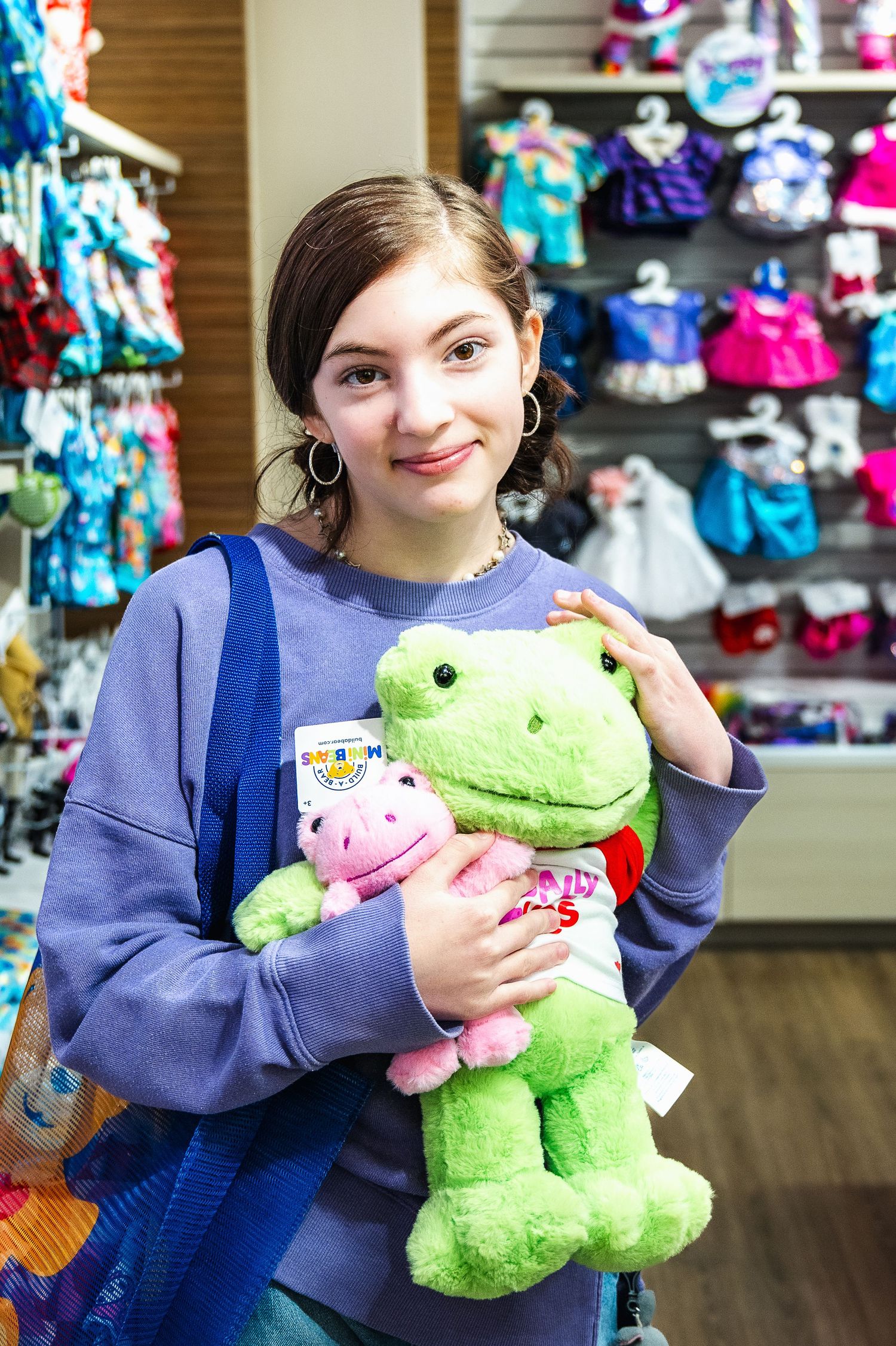 A person holds plush toys including a green frog and pink animal while shopping in a retail store.