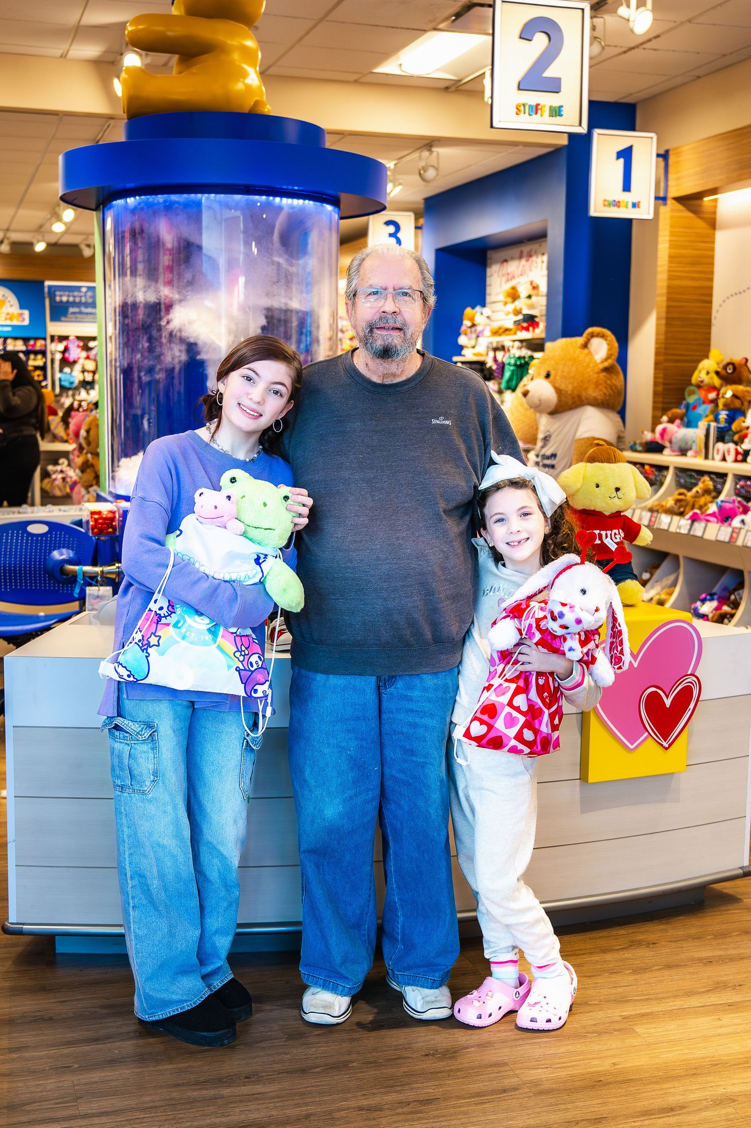 Three people stand together holding stuffed animals inside a Build-A-Bear Workshop retail store.