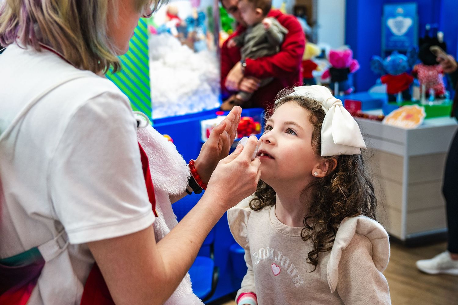 Child getting their face painted at a holiday event with blue walls and festive decorations in the background.