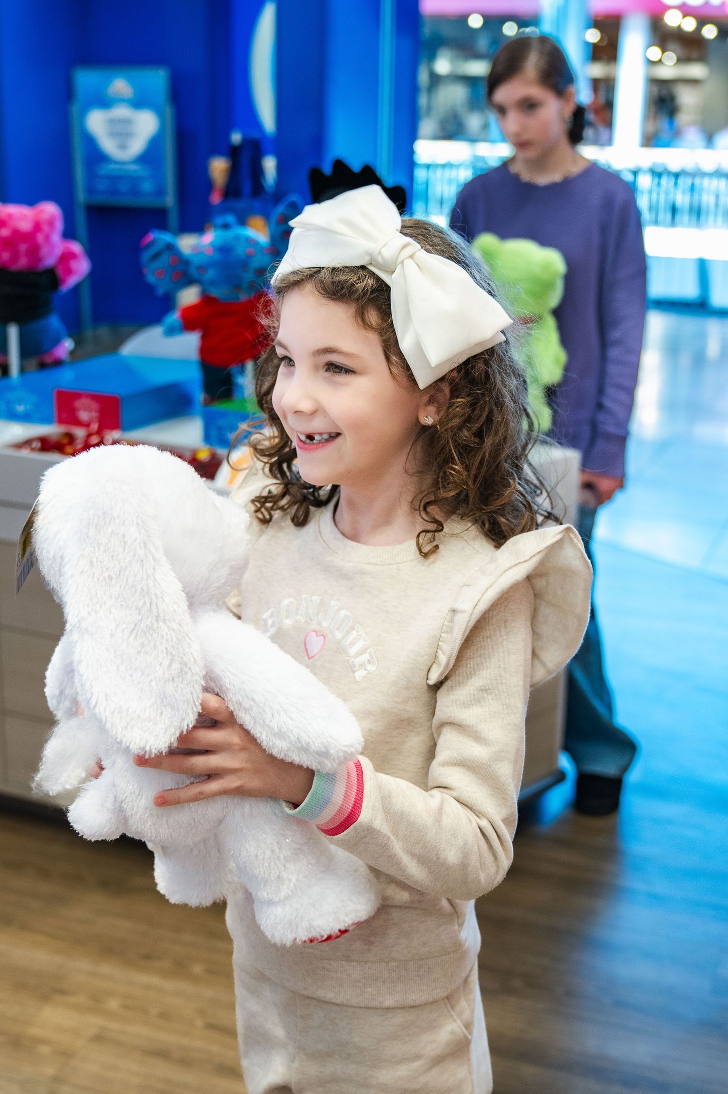 A young customer holds a white plush toy while shopping at a store filled with colorful stuffed animals.