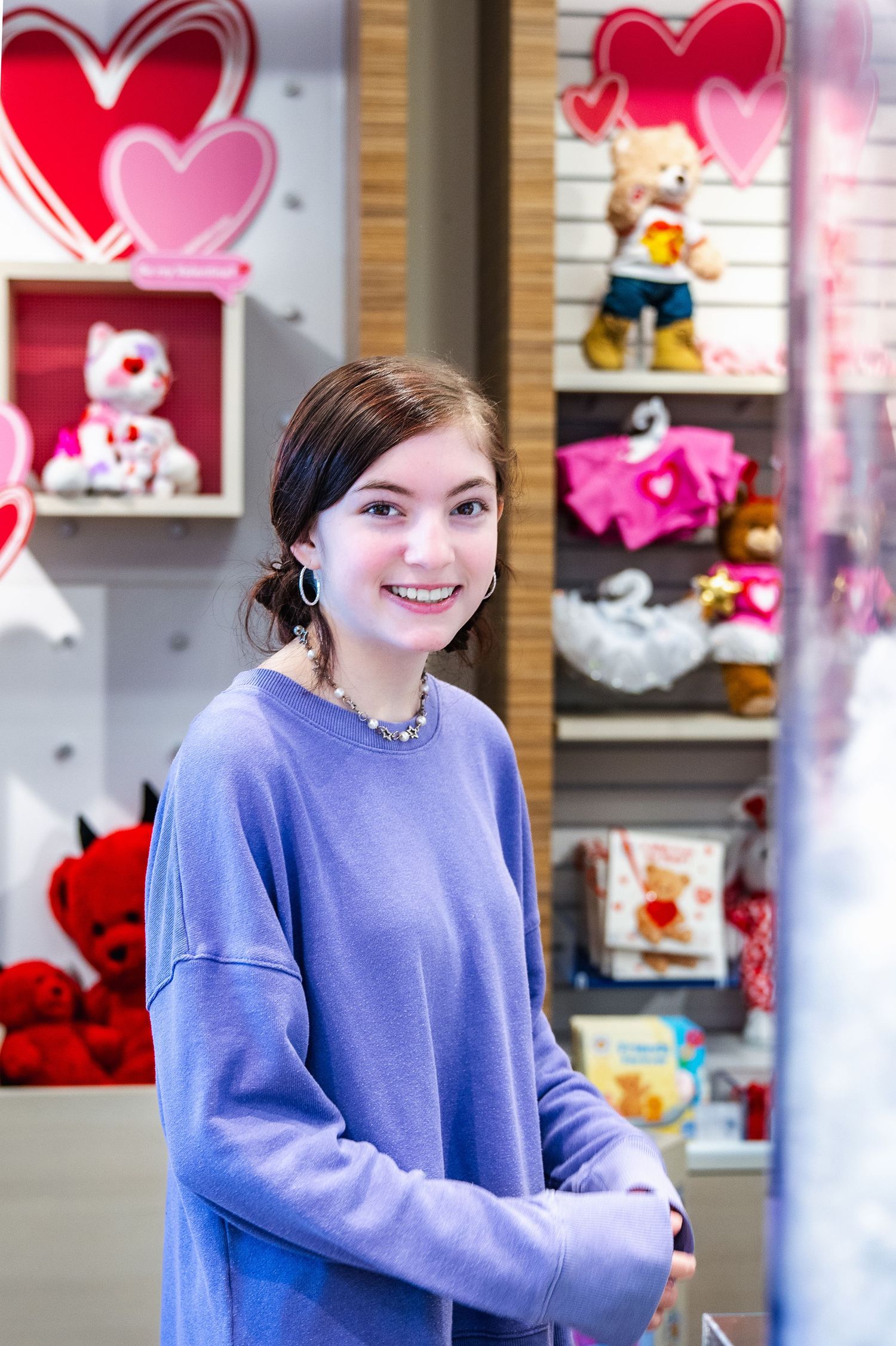 Person in lavender sweater stands in front of Valentine's Day retail display with hearts and plush toys.