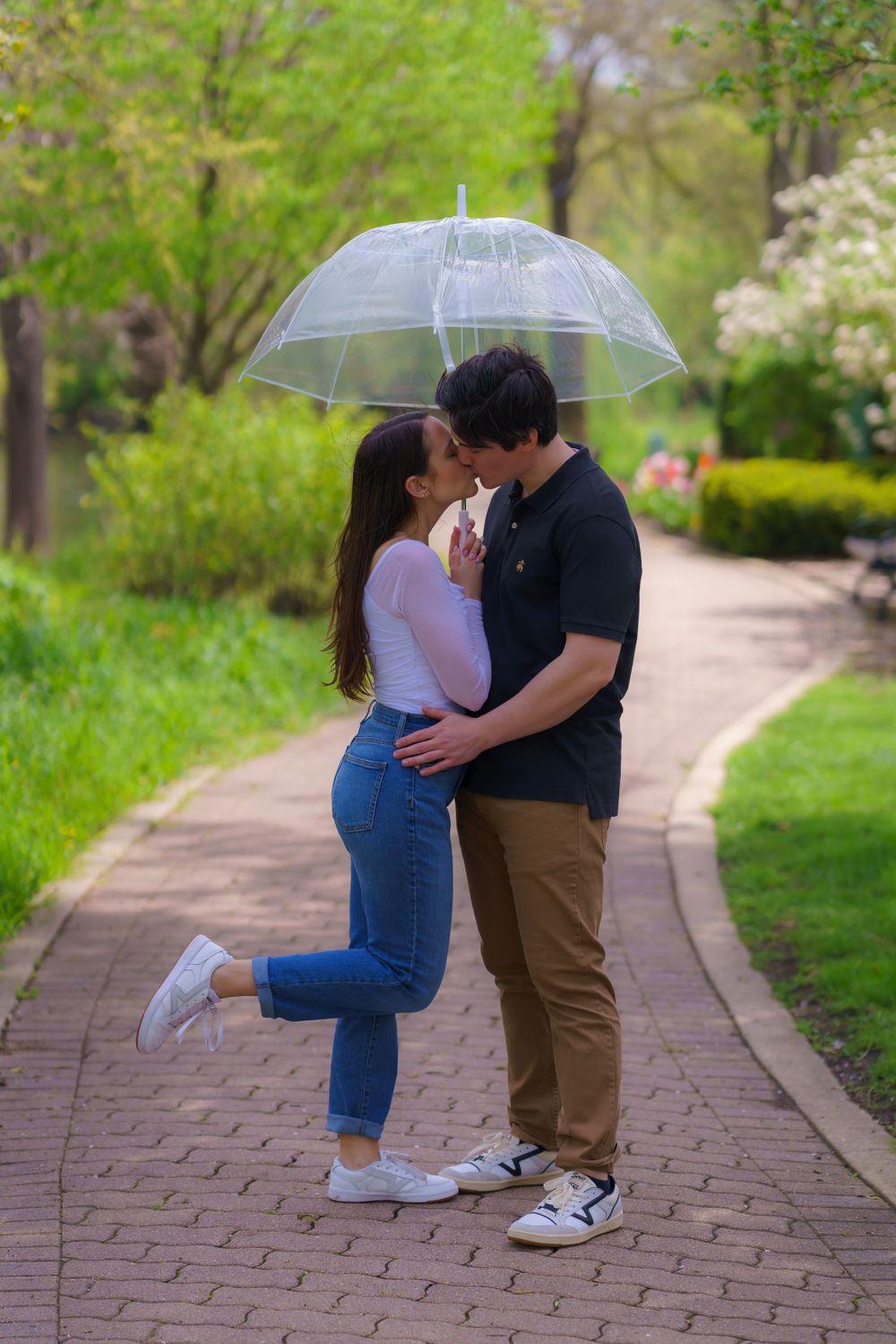 A romantic couple embraces on a brick pathway surrounded by spring greenery.